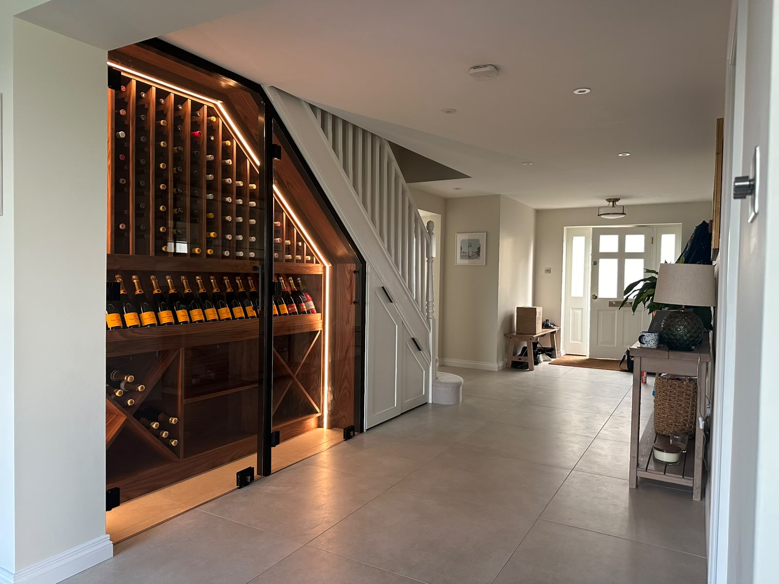 Bespoke under-stairs walnut wine cellar with glazed doors and integrated lighting in a hallway