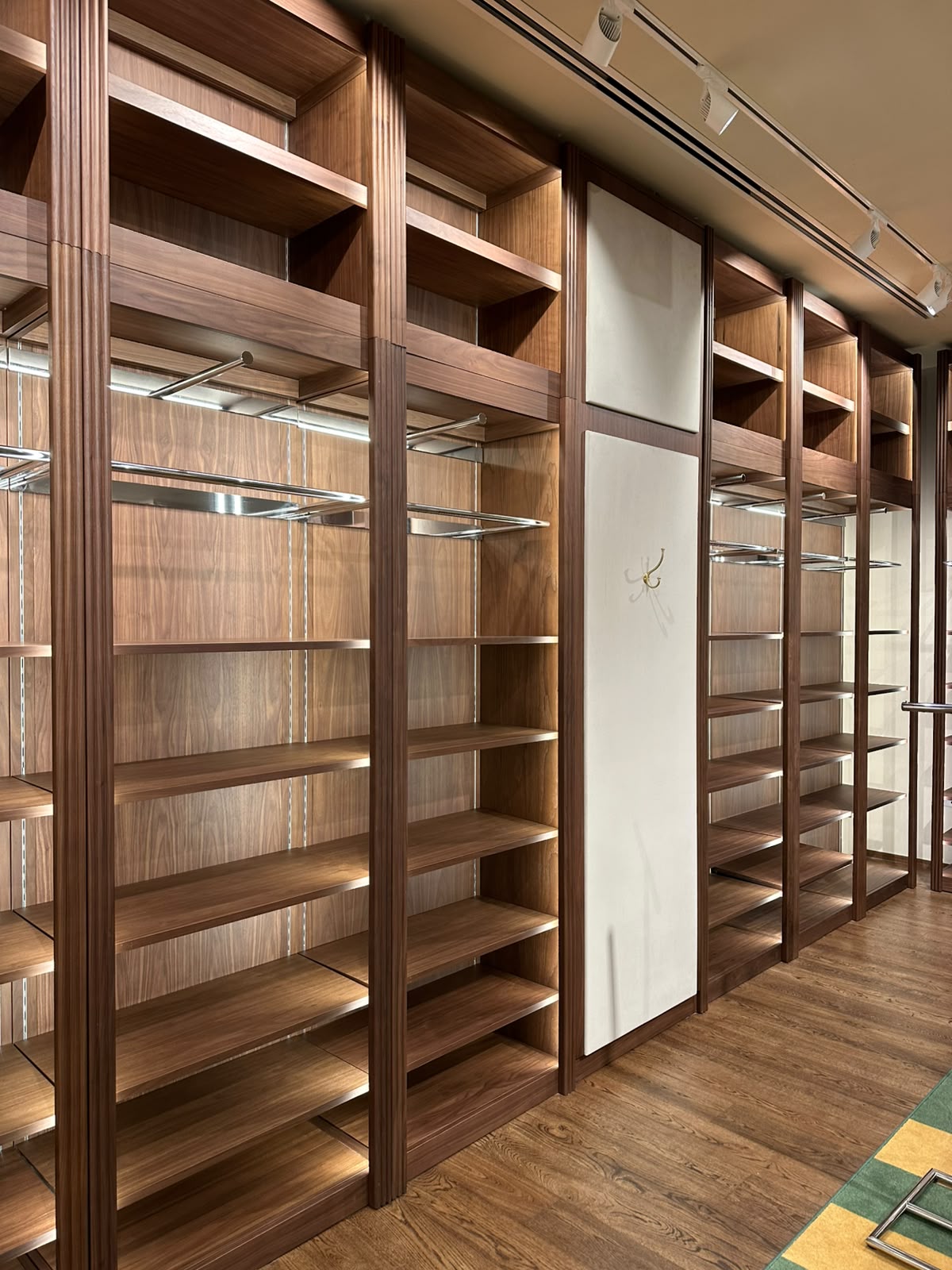 Full-height walnut fitted wardrobe run with open shelving, hanging rails and integrated lighting