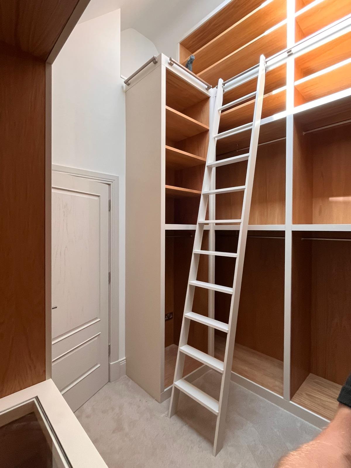 Fitted dressing room with oak-lined storage, hanging rails, illuminated shelving and a painted library ladder