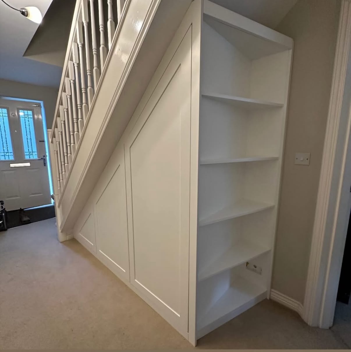 White painted under-stairs cupboards and shelving in a bright hallway