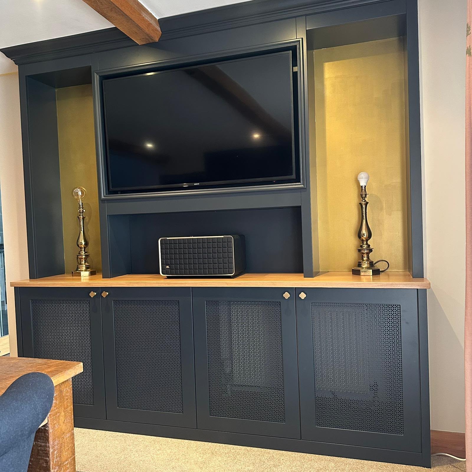 Navy bespoke media wall with a framed television, gold-lit alcoves, oak top and mesh-fronted media cupboards
