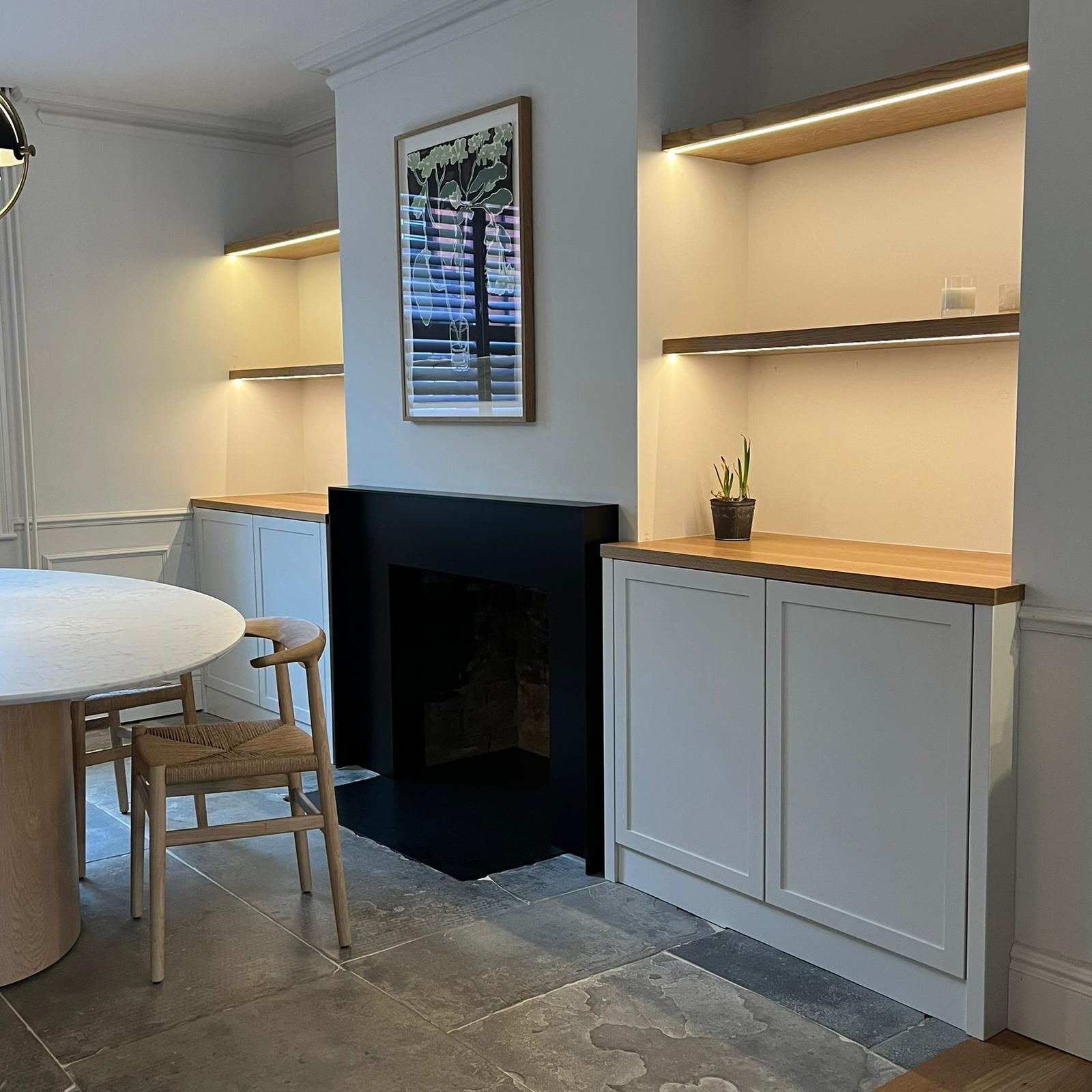 Painted alcove fitted furniture either side of a fireplace with timber shelves and integrated lighting