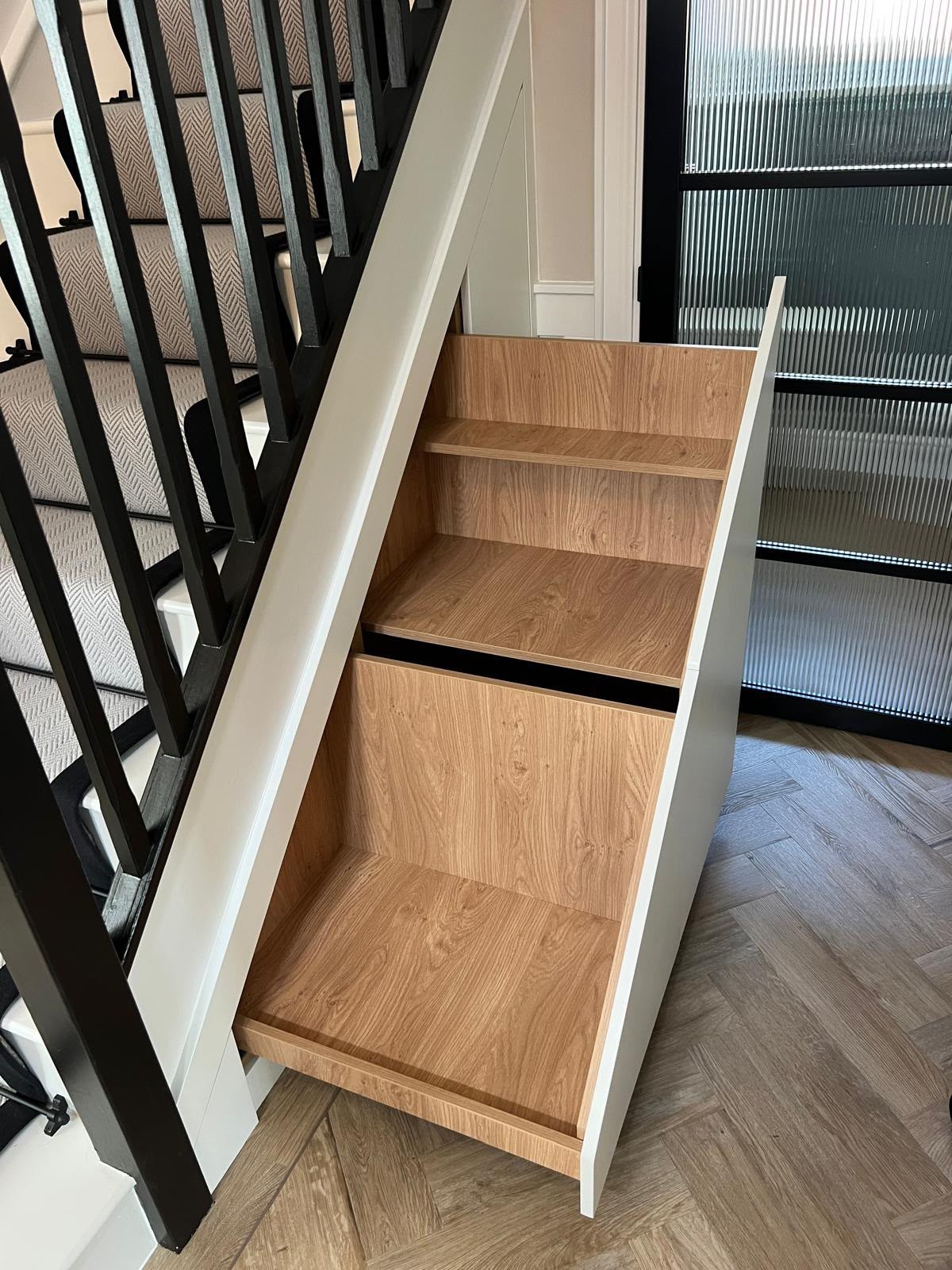 Open timber under-stairs drawers and shelving fitted beneath a staircase with black balustrades