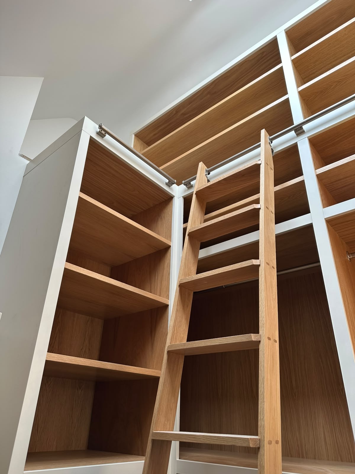 Bespoke dressing room with oak-lined open shelving, chrome hanging rails and a solid oak library ladder