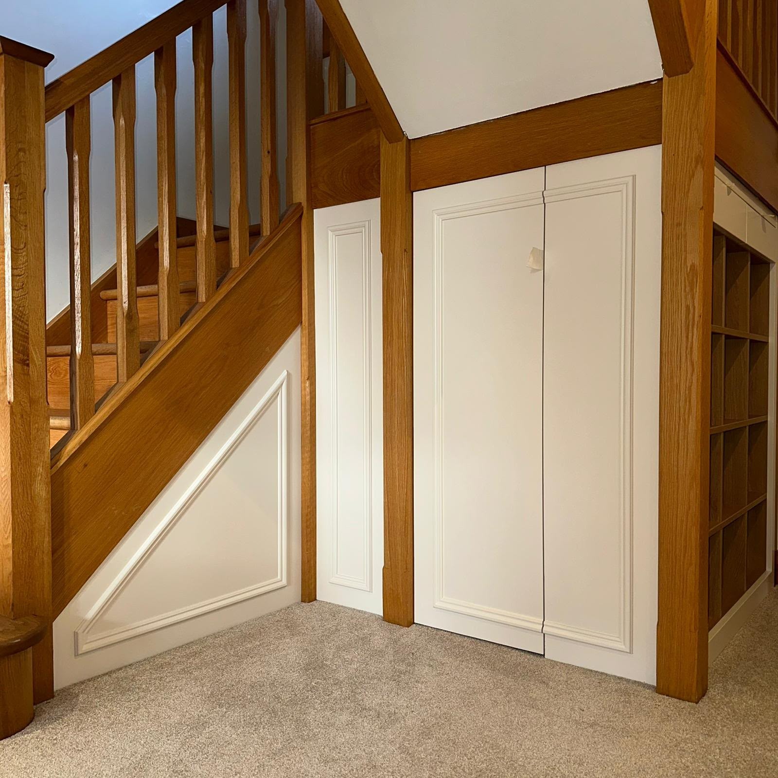 Painted under-stairs storage cupboards and open shelving beneath a traditional oak staircase