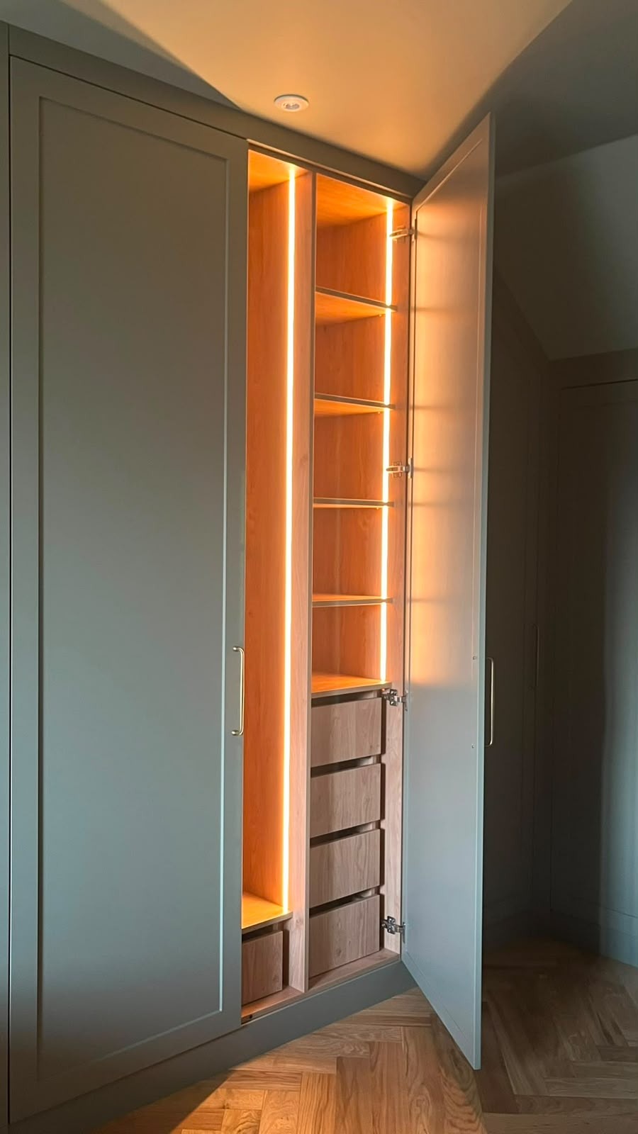 Tall bespoke fitted wardrobe with illuminated walnut shelving and soft-close drawers