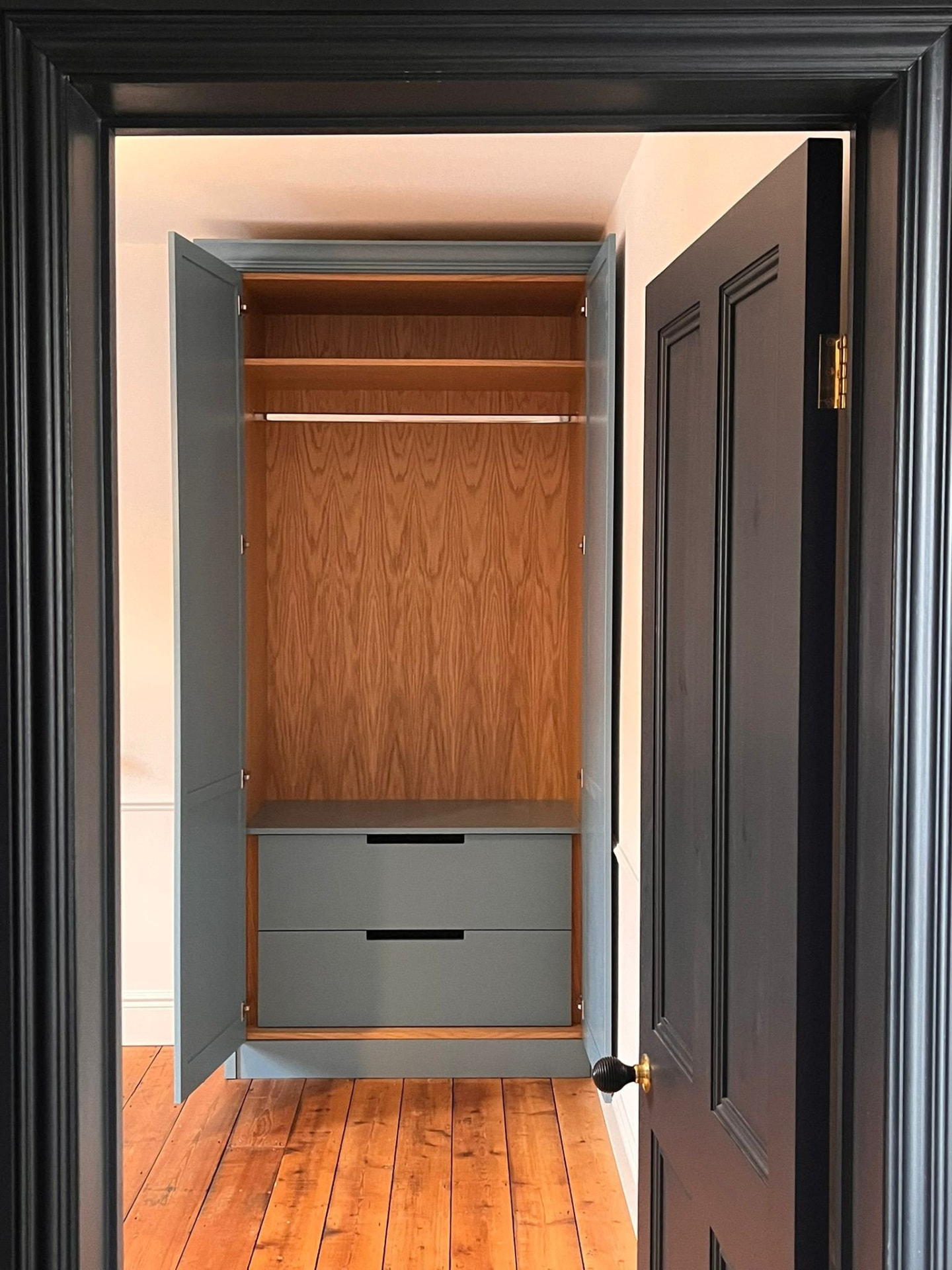 Compact dark-painted fitted wardrobe with walnut lining, hanging rail and drawers