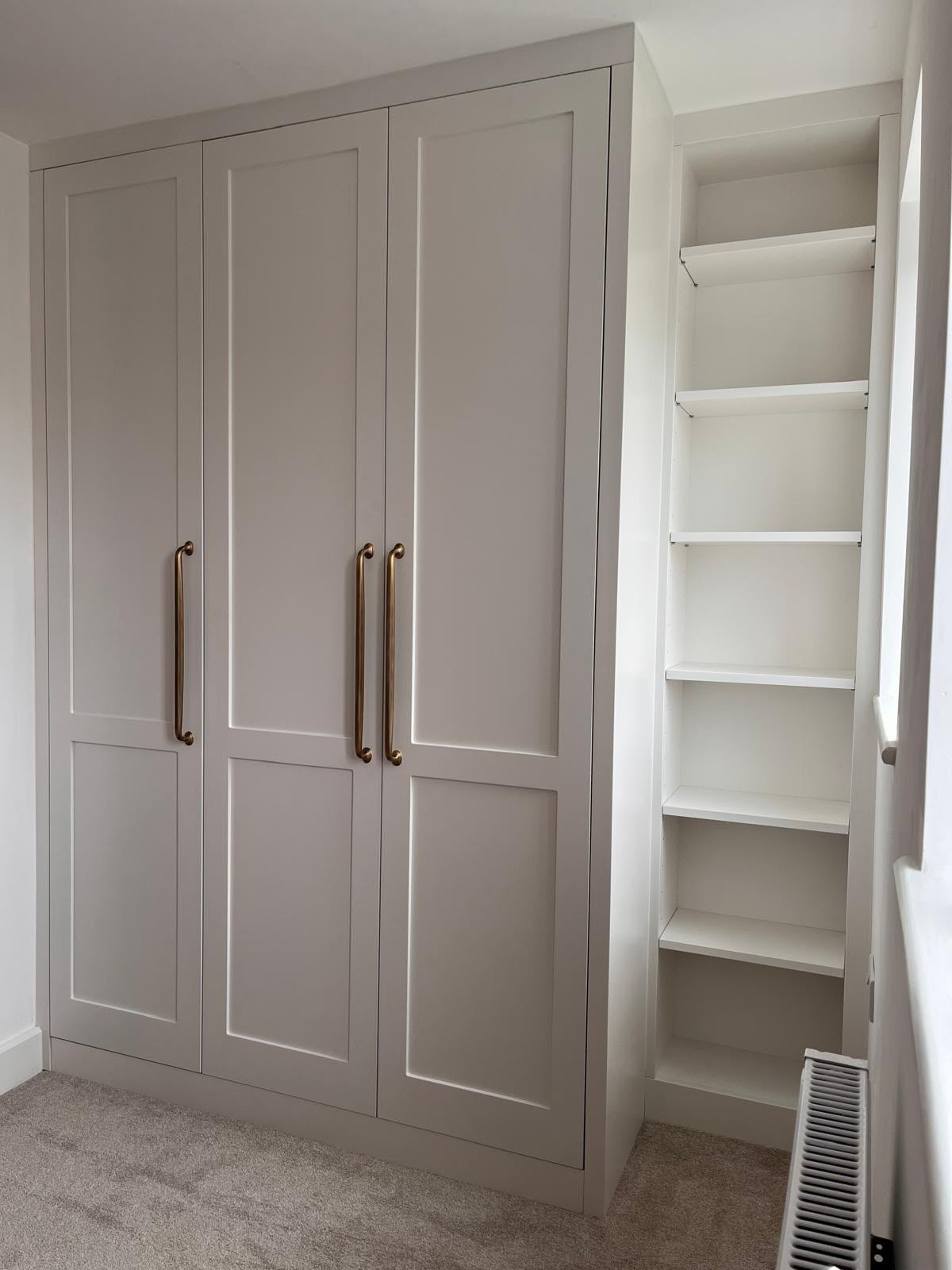 Pale hand-painted fitted wardrobe with brass handles and a tall open shelving bay
