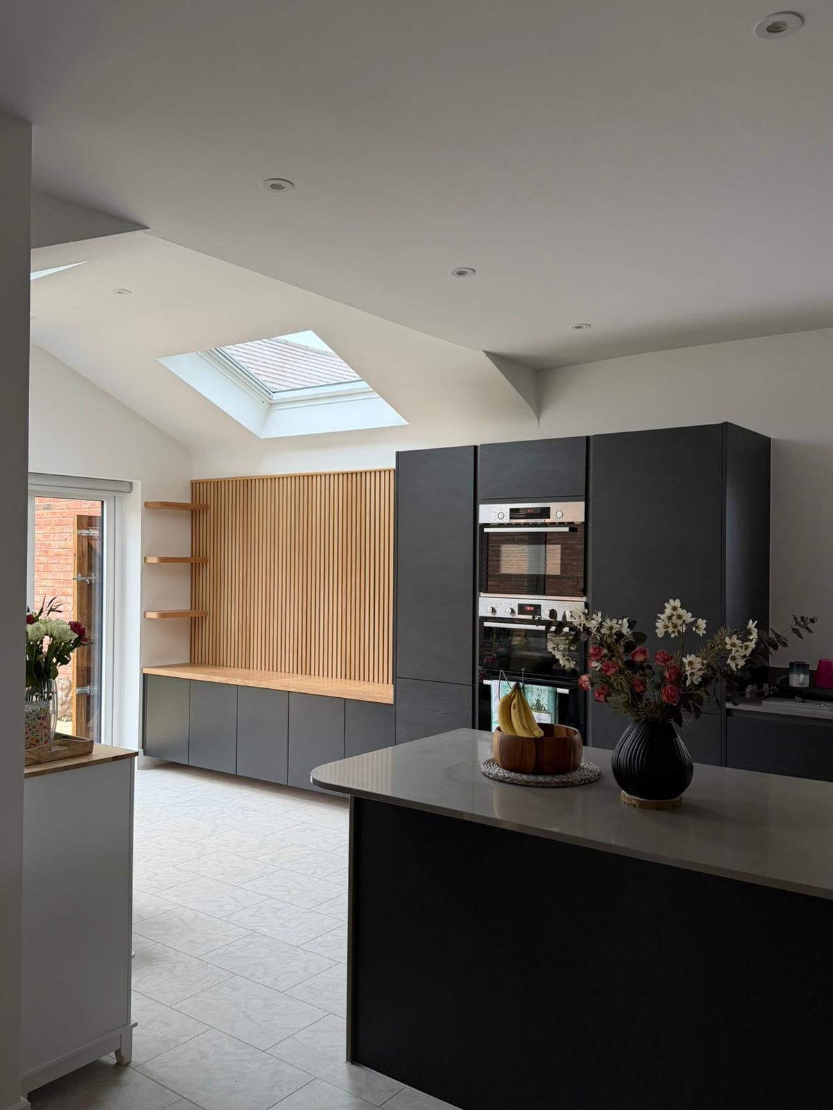 Contemporary dark bespoke kitchen with black cabinetry, integrated appliances and oak slatted wall panelling