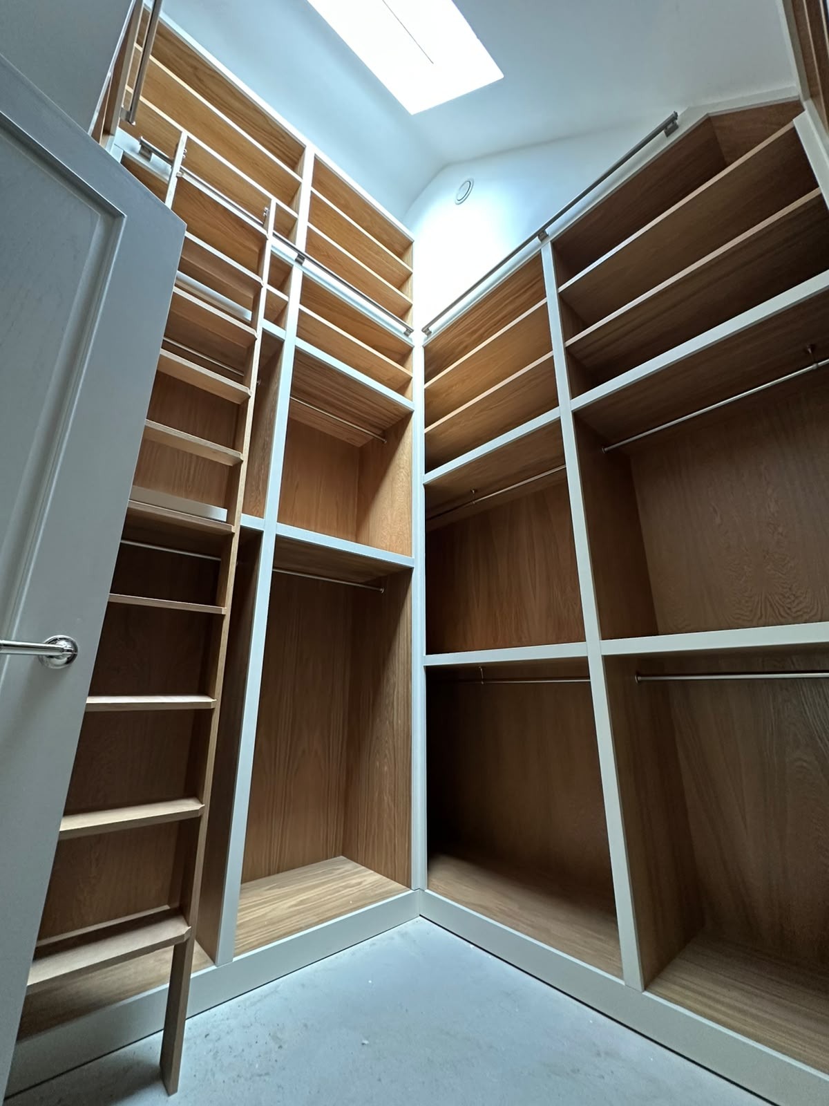 Bright walk-in dressing room with painted framing and oak interiors beneath a skylight